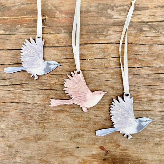 Three superb fairywren  ornaments displayed on a rustic wooden surface, each attached to a cream ribbon.