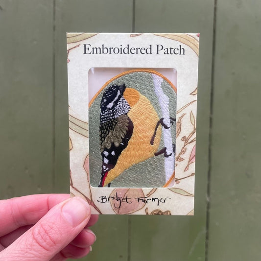 Embroidered patch in packaging held by a hand against a green background