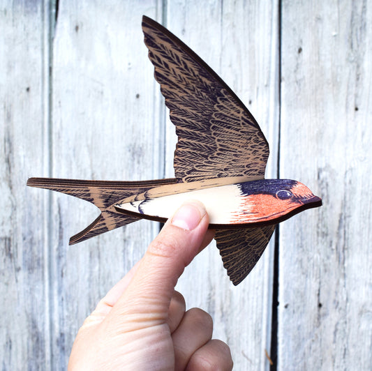 A hand holding a small wooden swallow figurine against a weathered gray wood plank background.